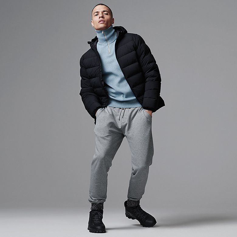 Man wearing blue half-zip jumper, grey joggers, black hooded puffer and chunky boots