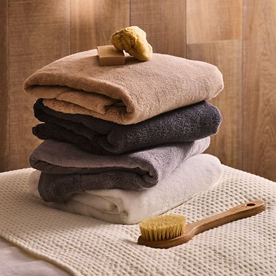 Folded stack of cotton towels with natural sponge and back brush. Shop the spa and wellness range