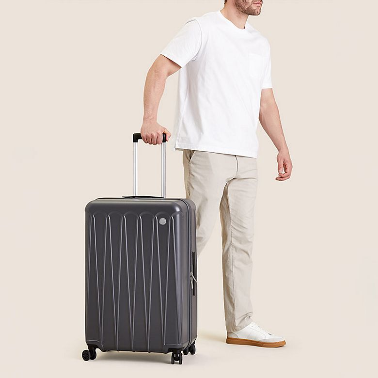 Man pulling a hardshell suitcase with wheels. Shop suitcases and luggage 