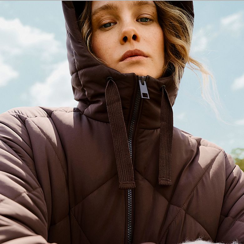 Woman wearing hooded brown padded duvet coat. Shop women’s puffer coats and jackets 