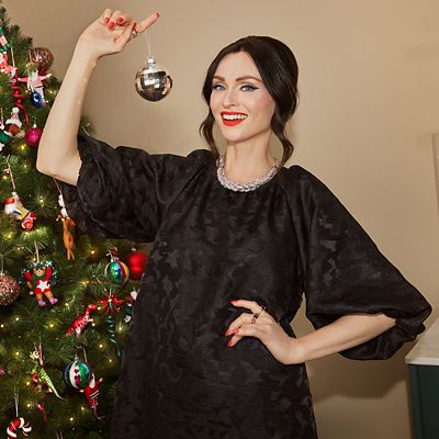 M&S Christmas advert star, Sophie Ellis-Bextor, wearing black puff-sleeve dress and silver necklace, holding a silver bauble beside a Christmas tree. Shop the M&S Christmas advert 