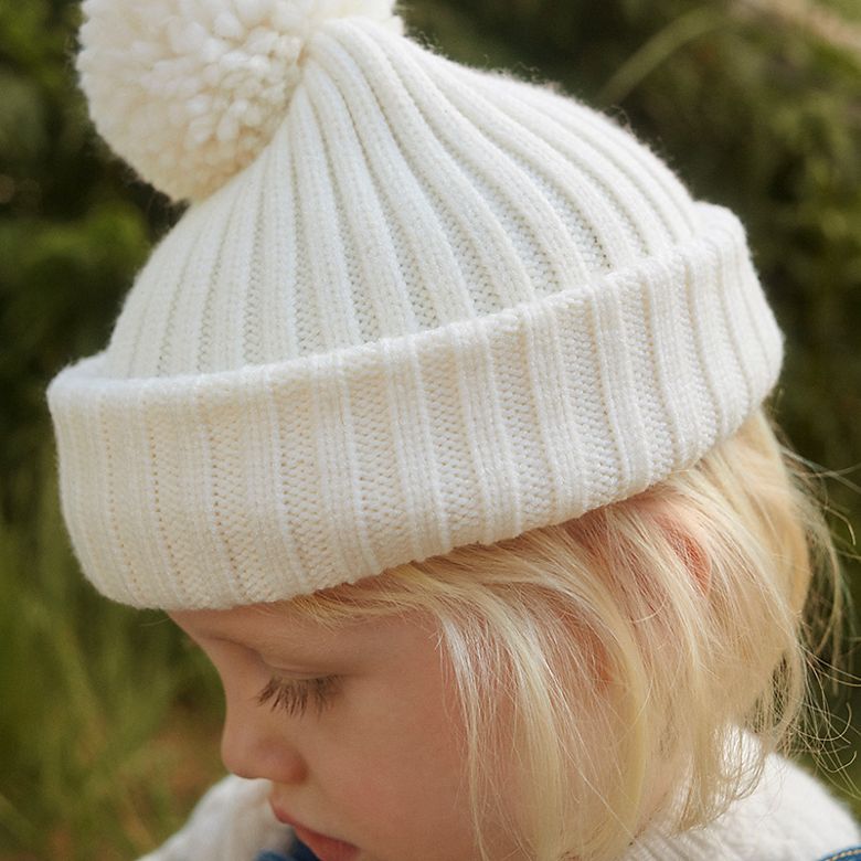 Girl wearing cream knitted hat. Shop girls’ accessories