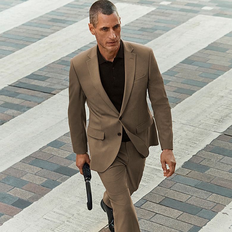 Man wearing light brown suit and black polo-shirt with black shoes. Shop men’s suits 