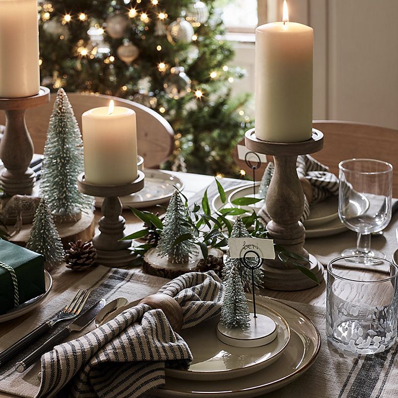 Christmas table set with cream crockery, candles in wooden holders and Christmas tree decorations