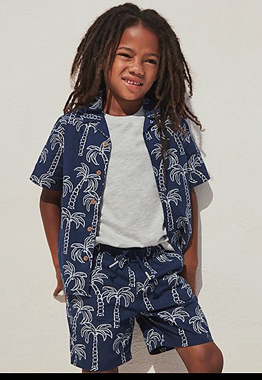 Boy wearing navy palm-print shirt and matching shorts. Shop boys’ shorts