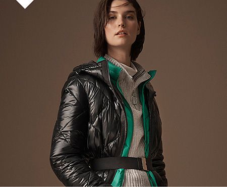 Model wears a black padded coat over a green padded jacket and grey ribbed jumper