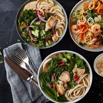 Bowls of chicken broth with noodles and stir-fried king prawns with noodles
