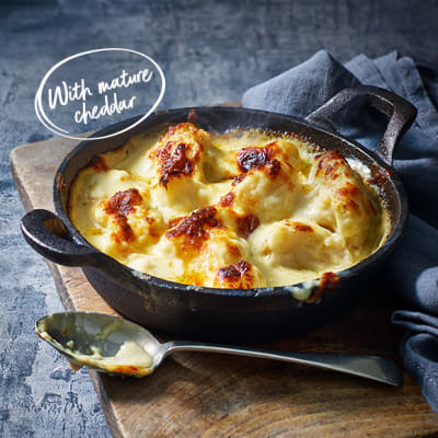 Baked cauliflower cheese with a golden brown topping in a cast iron pan