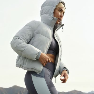 Woman wearing grey puffer jacket, sports bra and leggings. Shop sportswear