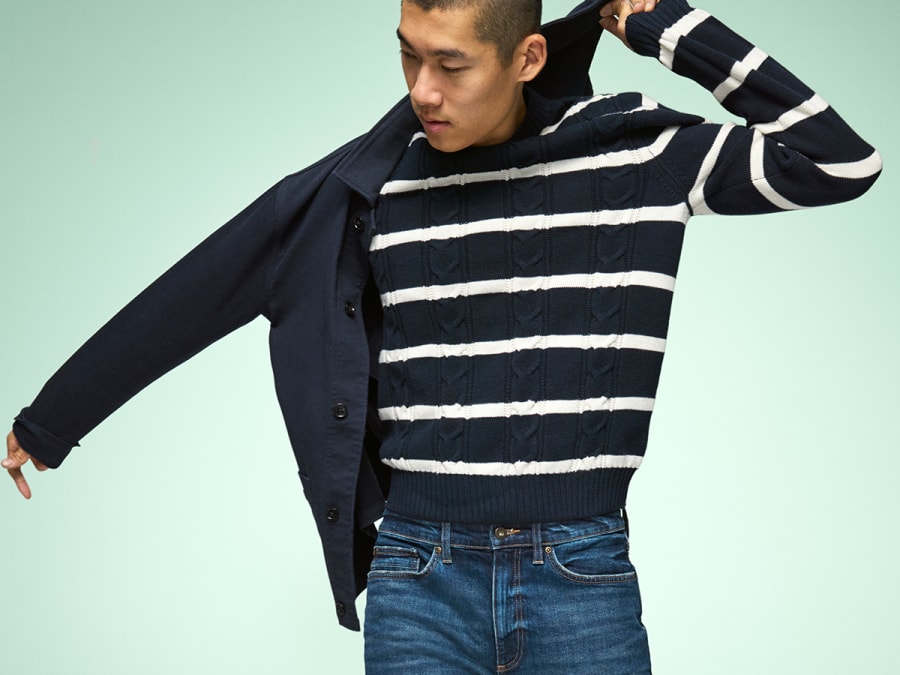 Man wearing dark-wash blue jeans, white long-sleeve top, white cap and black trainers 