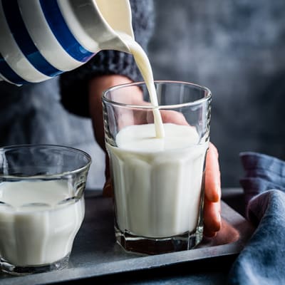 Glass of milk and milk being poured from a jug into a glass