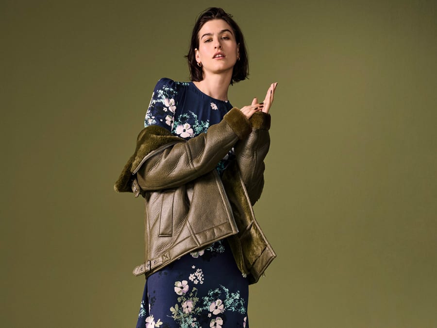 Woman wearing floral dress and faux leather jacket. Shop 30% off selected coats