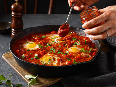 A tray of shakshuka with a person spooning in M&S smoked tomato paste