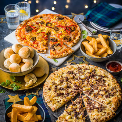 Two pizzas, garlic dough balls and chunky chips on serving plates