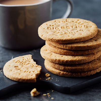 Stack of M&S digestive biscuits on black slate with cup of tea in background