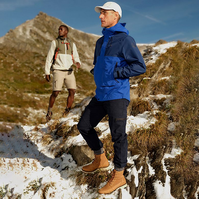 Man wearing blue anorak, black trousers and brown hiking boots. Shop Trek at Goodmove