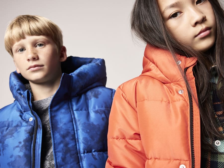 Boy and girl wearing bright padded coats. Shop kids’ coats