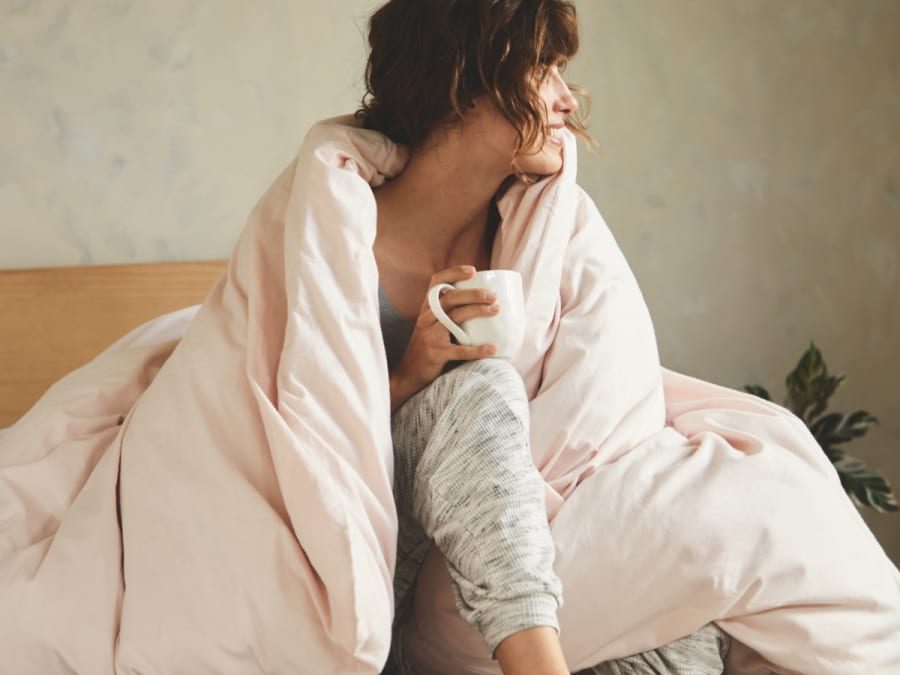 Woman sitting on bed wrapped in a duvet. Make your home more cosy