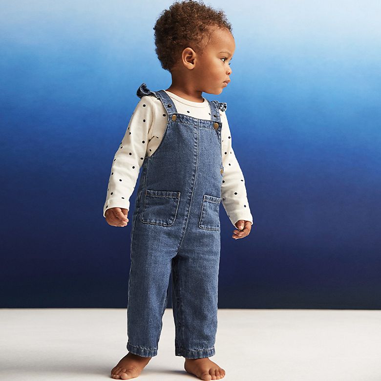 Toddler wearing denim dungarees and long-sleeved polka-dot top with bare feet