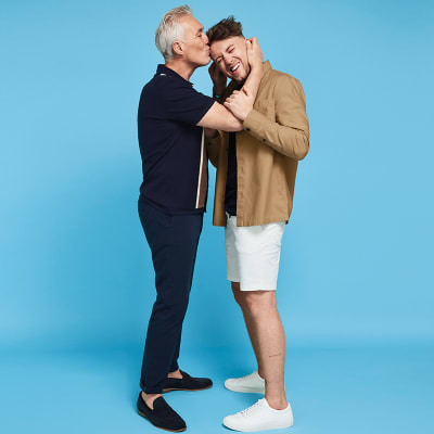 Martin Kemp wearing a polo shirt and navy trousers with Roman Kemp wearing a black T-shirt, ecru overshirt and white shorts