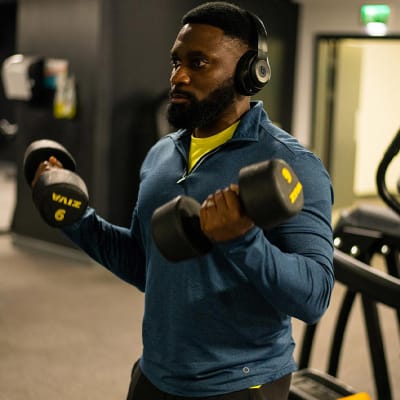Man wearing zip-up top, yellow T-shirt and black leggings to lift weights