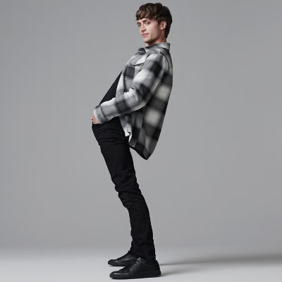 Man wearing black jeans, black and white checked overshirt and black shoes