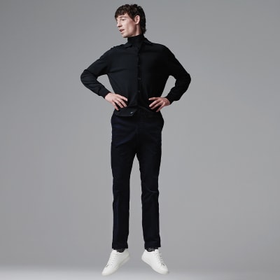 Man wearing black merino-wool roll-neck, black cardigan, black cords and white trainers