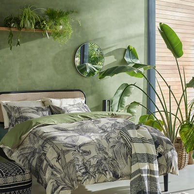 Bedroom with cane double bed, palm-print bed linen and lots of plants