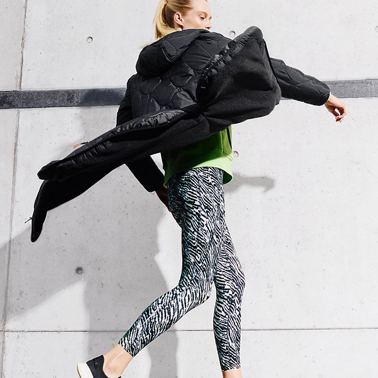 Woman running wearing Goodmove black quilted jacket and patterned leggings. Shop Goodmove winter gym clothes