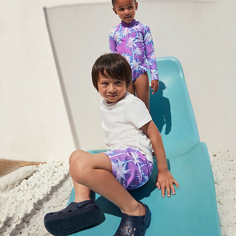 Boy and girl wearing summer holiday clothing. Shop kids’ holiday clothes
