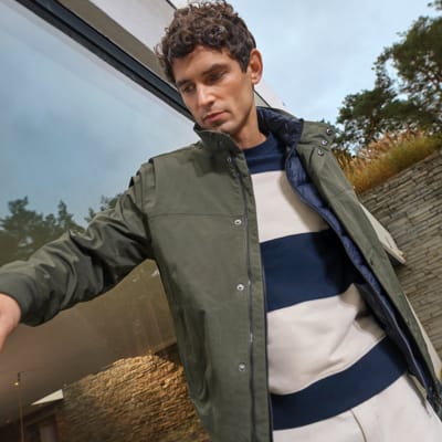Man wearing khaki bomber jacket, white and navy striped sweatshirt and ecru jeans. Shop men’s new in