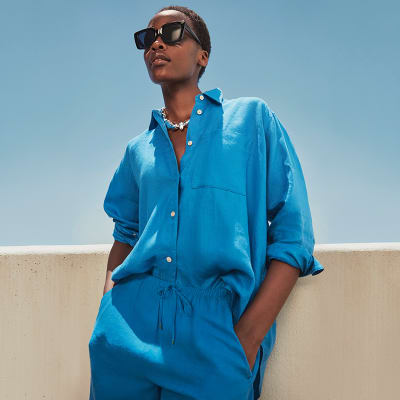 Woman wearing bright blue linen button-down shirt and wide-leg trousers. Visit the linen shop