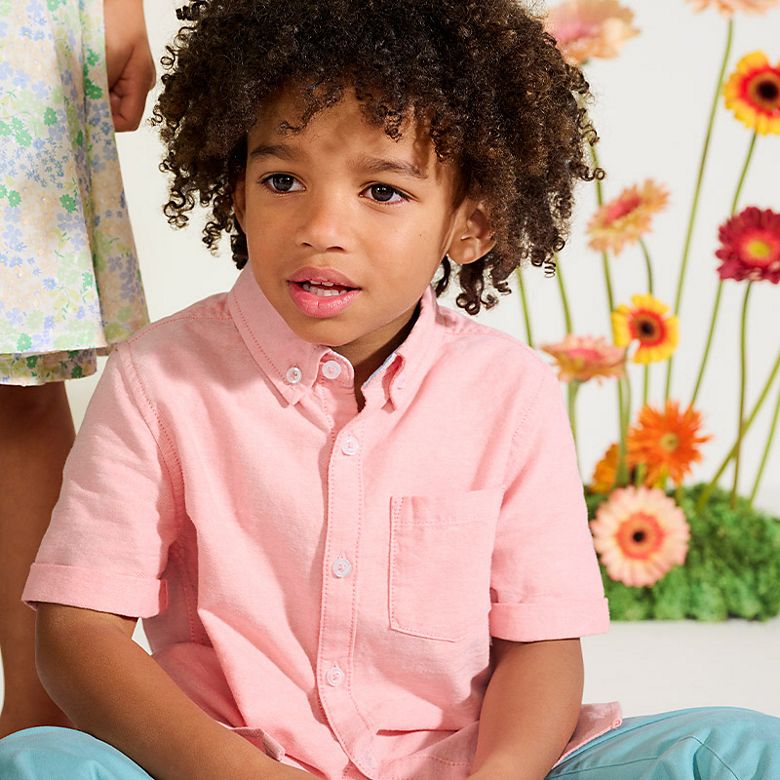 Boy wearing a pink shirt and blue chinos. Shop kids’ new in. 