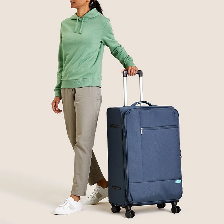 Woman pulling a soft-shell suitcase with wheels. Shop suitcases and luggage 