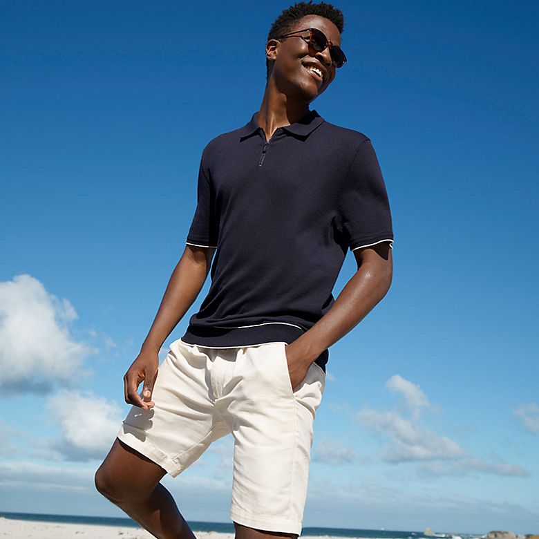 Man wearing navy polo shirt, white shorts and sunglasses. Shop polo shirts. 