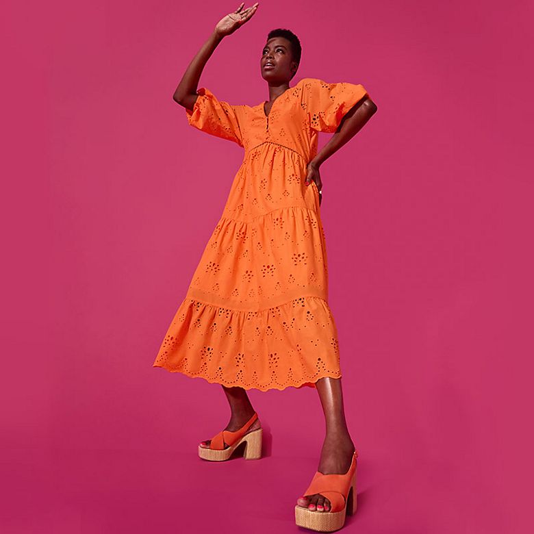 Woman wearing a bright orange summer dress. Shop now. 