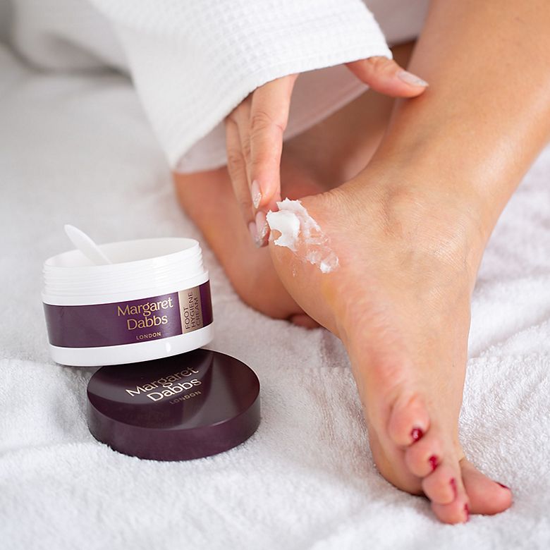 Woman rubbing cream into bare feet. Shop nail care products. 