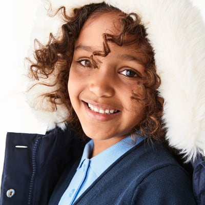 Girl wearing navy coat with faux fur trim and school uniform. Shop girls’ school uniform 