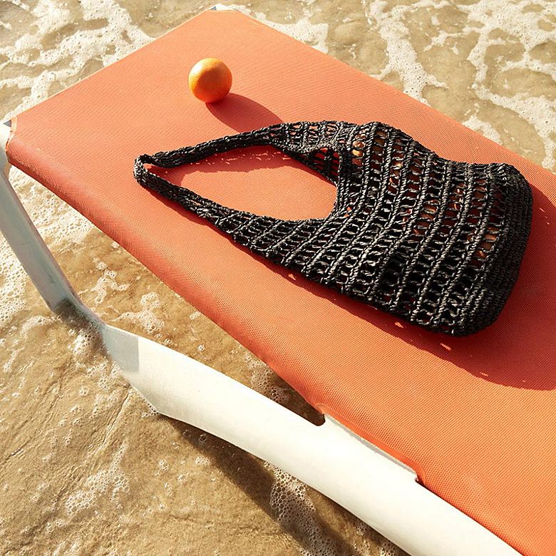 Woven beach bag on a sun lounger. Shop women’s handbags 