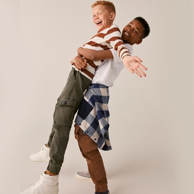 Boys wearing M&S summer daywear including stripes tops and cargo trousers. Shop boys’ clothing.