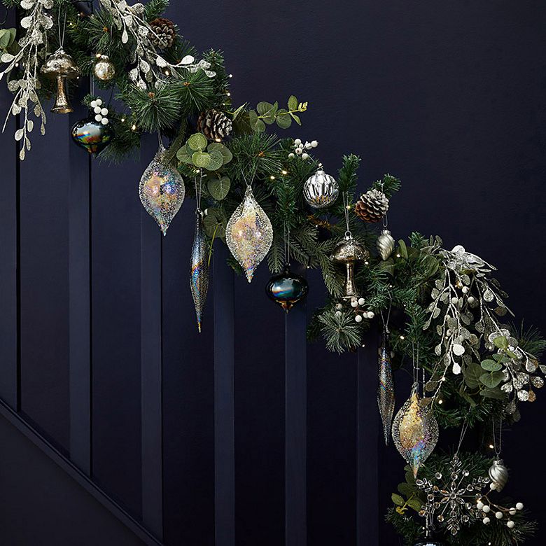 Bannister decorated with a Christmas garland featuring glass baubles, silver sprigs, toadstool ornaments and beaded stars. Shop Christmas decorations 