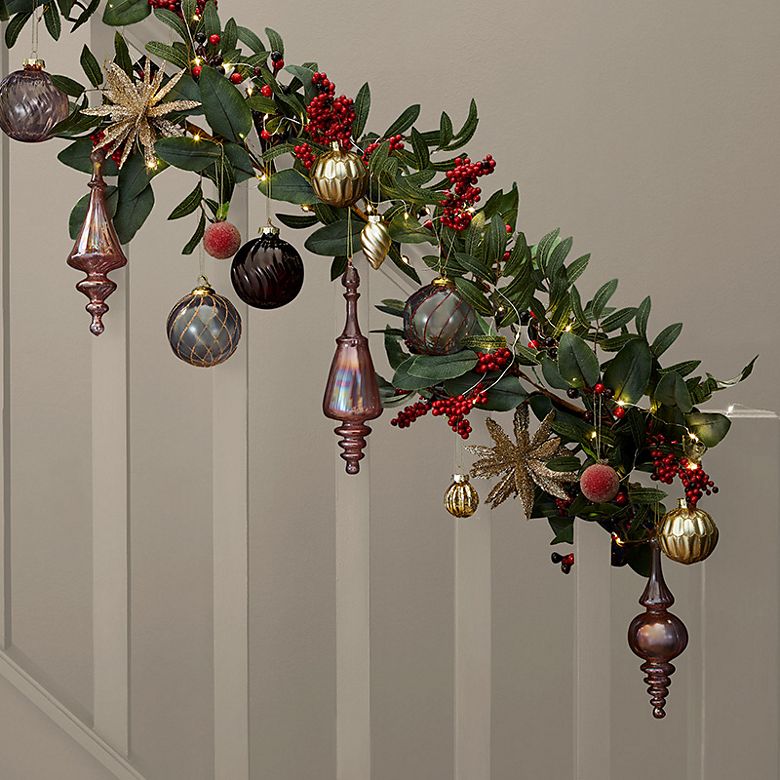 Bannister decorated with a Christmas garland featuring red berries, iridescent glass baubles and gold stars. Shop Christmas decorations 