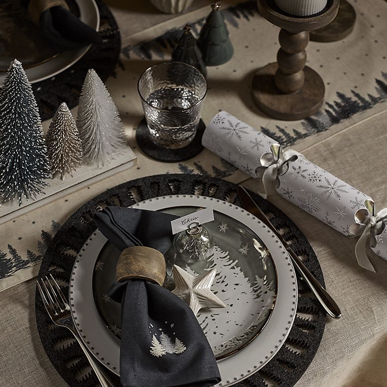 Christmas table set with decorative crockery, candles in wooden holders and decorative Christmas trees. Shop Christmas tableware 