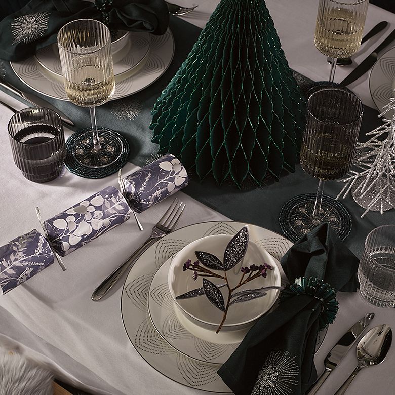 Christmas table set with crepe paper trees, white and silver crockery and festive greenery. Shop christmas tableware 
