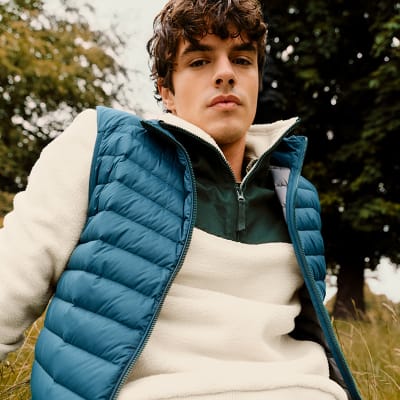 Man wearing white fleece and blue quilted gilet. Shop men’s padded gilets