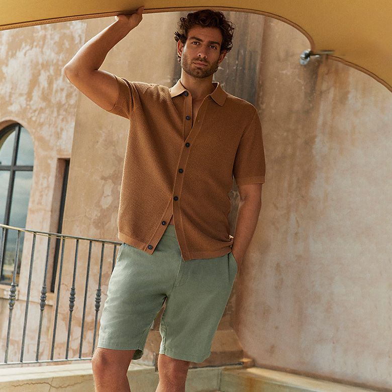 Man wearing a light brown button-down polo shirt, faded aqua chino shorts. Shop men’s chino shorts