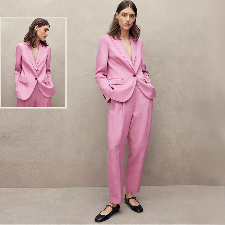Woman wearing pink trouser suit by Jaeger with black Mary Jane shoes. Shop women’s suits. 