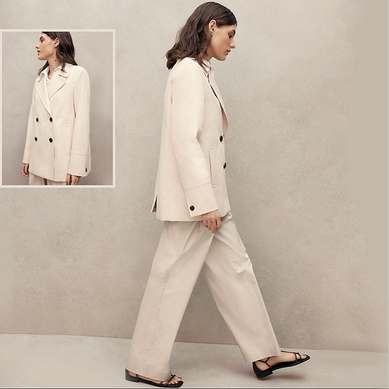 Woman wearing beige double-breasted trouser suit by Jaeger. Shop women’s suits.