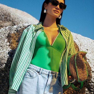 Woman wearing a green swimsuit, green striped shirt and light-blue wide-leg jeans. Shop women’s summer clothing