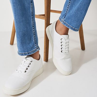 Woman wearing blue jeans and white lace-up trainers. Shop women’s white trainers